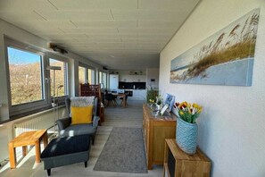 A spacious living area with a sofa, ottoman, and a coffee table. There is a painting on the wall and a vase with flowers on a side table. - Sea lavender in the house Sea greeting (Juist)