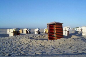 A row of beach huts with numbers on them, arranged on a sandy beach. - Sea lavender in the house Sea greeting (Juist)