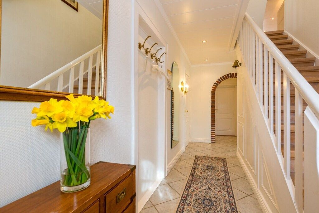 A hallway with a wooden staircase, a mirror, and a vase of yellow flowers on a wooden dresser.
