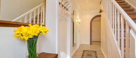 A hallway with a wooden staircase, a mirror, and a vase of yellow flowers on a wooden dresser.