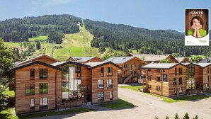 Moderni hotellikompleksi, jossa on useita puurakennuksia, pysäköintialue ja vuoristomaisema taustalla.
