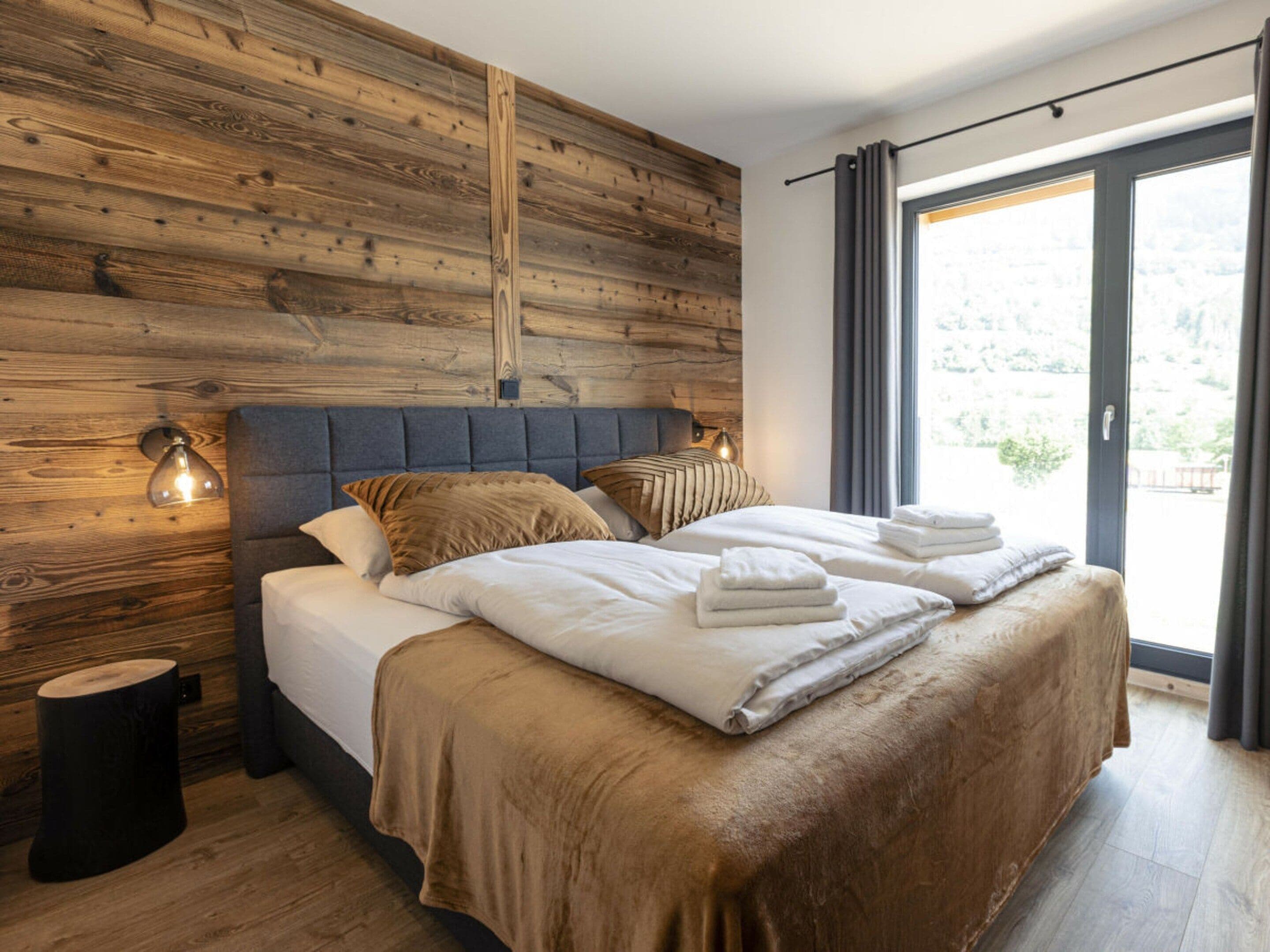 A modern bedroom with a wooden headboard, a large bed with white linens, and a view through a sliding glass door.
