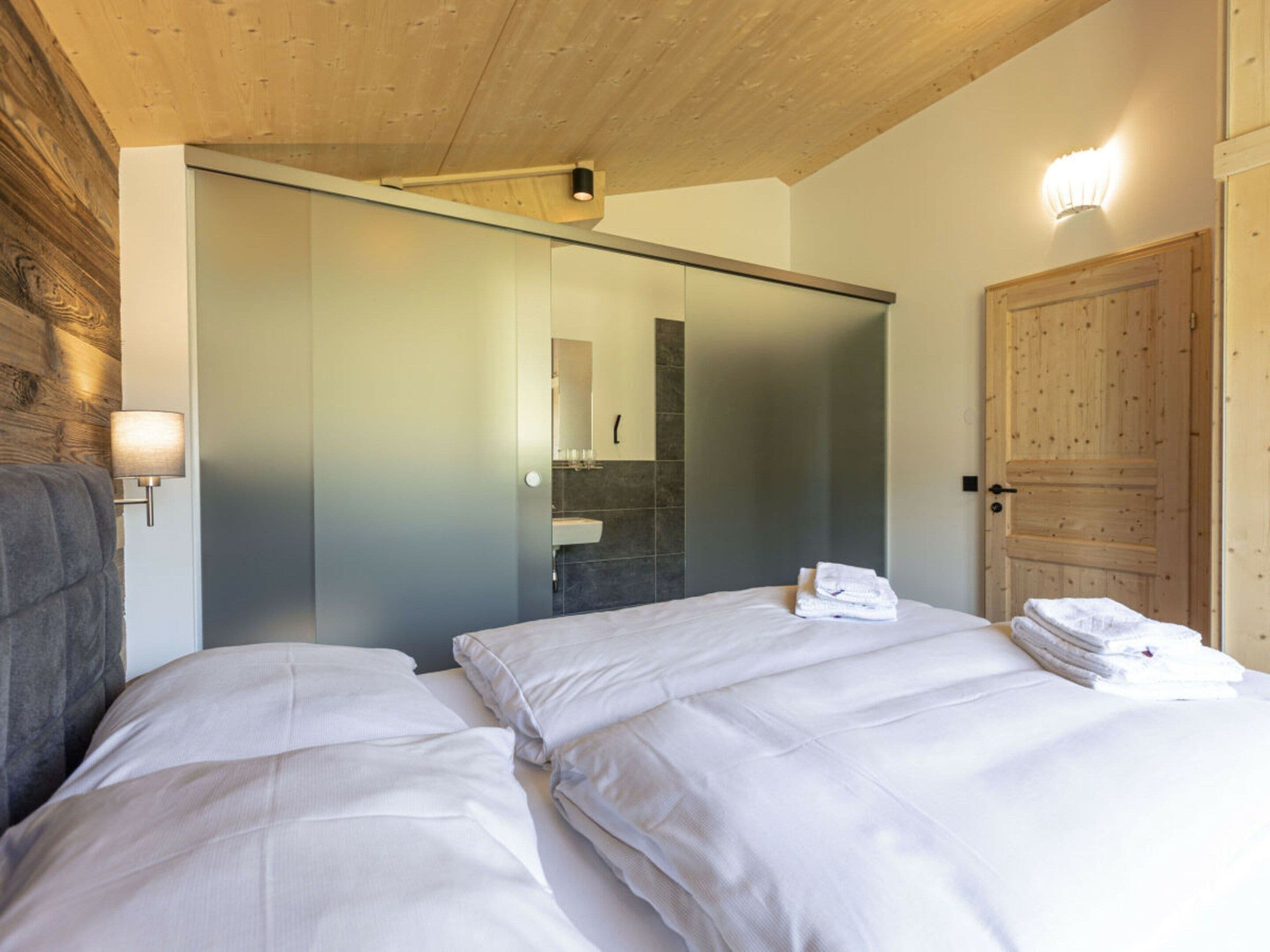 Un dormitorio con dos camas, techo de madera, armario con puerta corredera, espejo de baño y una pila de toallas.