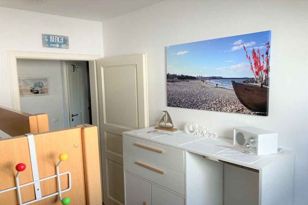 Ein Zimmer mit einem Strandgemälde, einem weißen Schreibtisch mit Schubladen und einer Tür zu einem weiteren Raum.