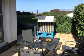 An outdoor patio with a table, chairs, and a blue and white striped lounge chair. - Holiday apartment in Glowe with swimming pool (Glowe)