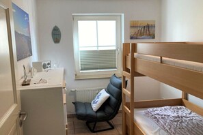 A room with a bunk bed, a desk with a chair, a radiator, and a window with blinds. - Holiday apartment in Glowe with swimming pool (Glowe)