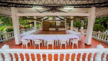 An outdoor covered patio with white columns and tables, surrounded by a white railing.
