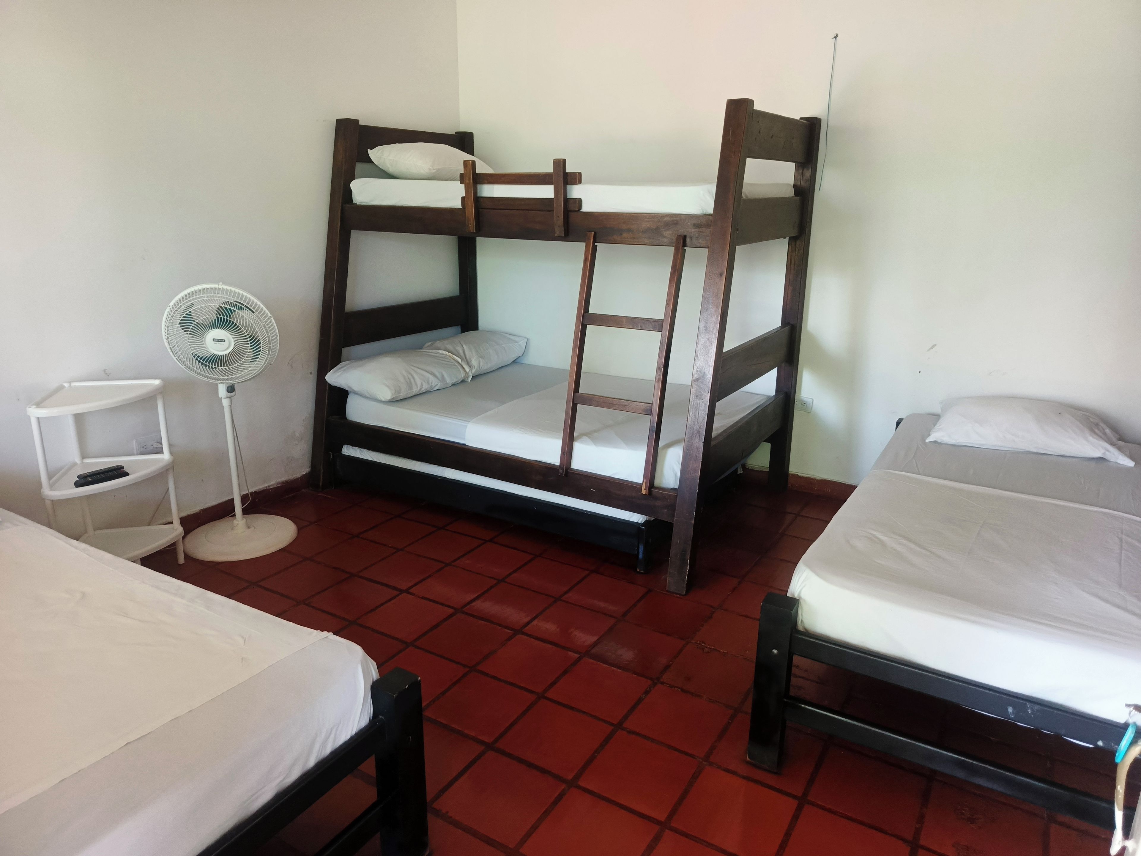A room with two bunk beds, a standing fan, and a white shelf unit.