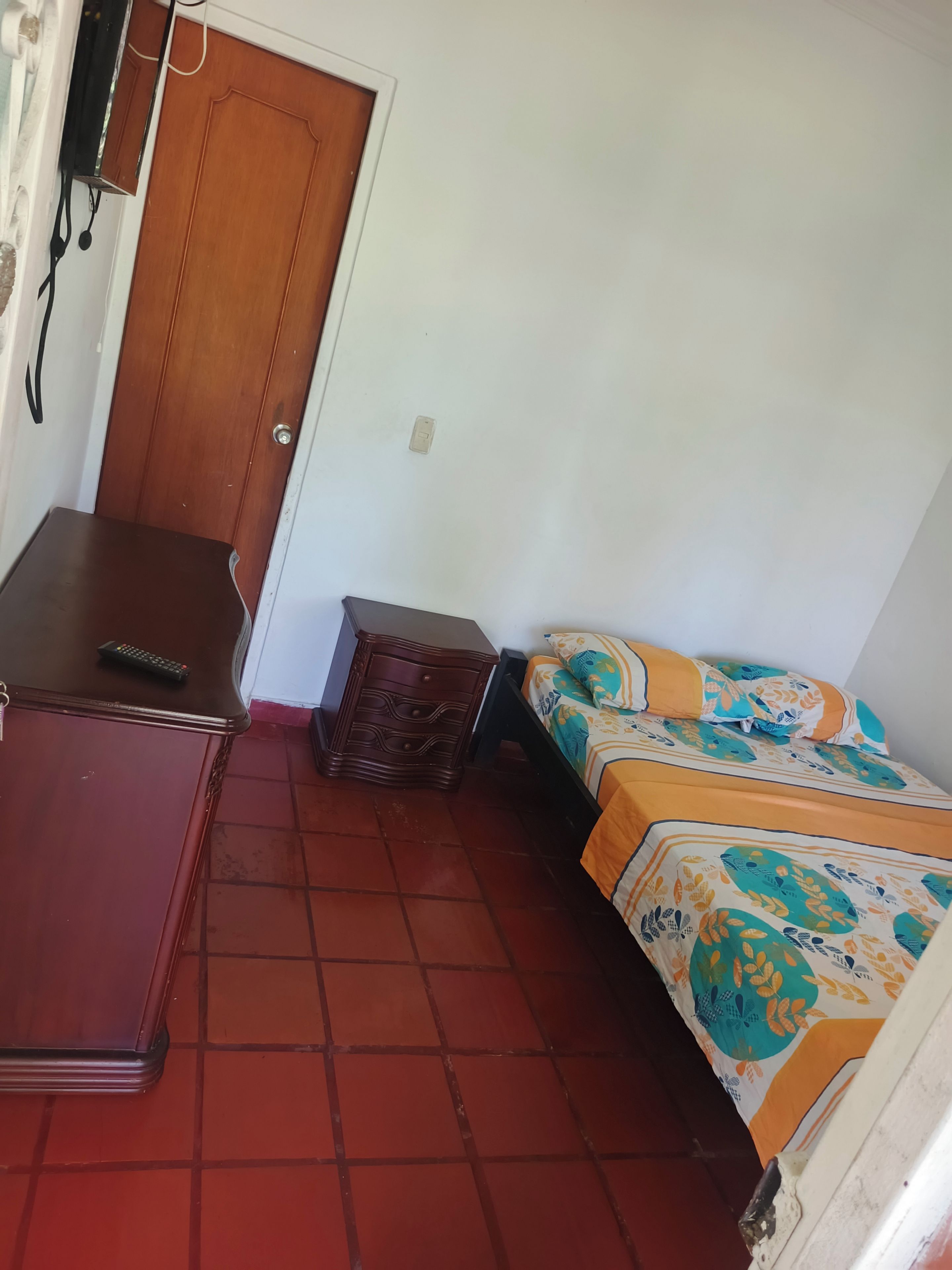 Een kamer met een bed, een klein houten kastje en een bureau met een afstandsbediening.
