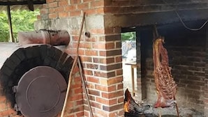 A brick oven with a chimney, a hanging meat rack, and a large metal door.