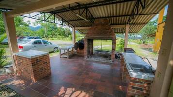 Un patio al aire libre con una zona de parrillada de ladrillo, un lavamanos y un área de estar cubierta.