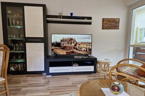 Een woonkamer met een televisie, een boekenkast en rieten meubels.