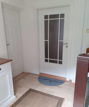 Een witte deur met een matglazen ruit, een deurmat met de tekst 'Welcome' en een houten vloer.