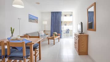 Ein modernes Wohnzimmer mit einer Couch, einem Esstisch und Stühlen. Ein Fernseher steht auf einem Holzschrank und ein Gemälde ist an der Wand zu sehen.