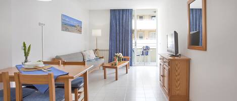 Una sala de estar moderna con sofá, mesa de comedor y sillas. Hay un televisor sobre un mueble de madera y un cuadro en la pared.