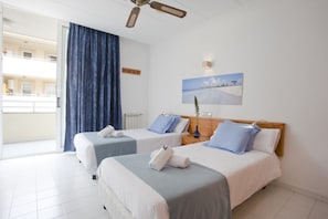 Habitación de hotel con dos camas, vista al mar, ventilador de techo y un cuadro en la pared.