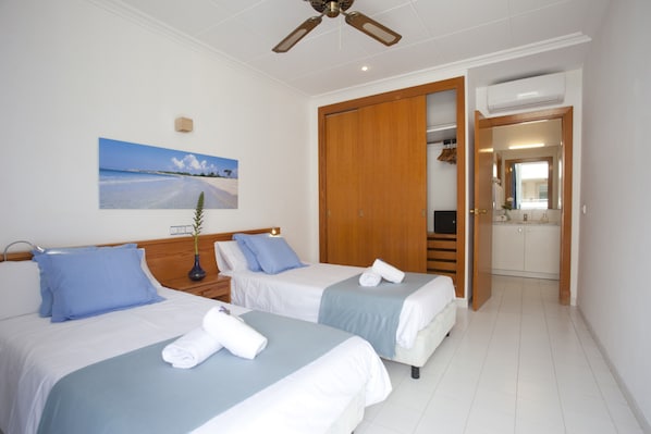 Habitación de hotel con dos camas, ventilador de techo, un cuadro de playa y un armario de madera.