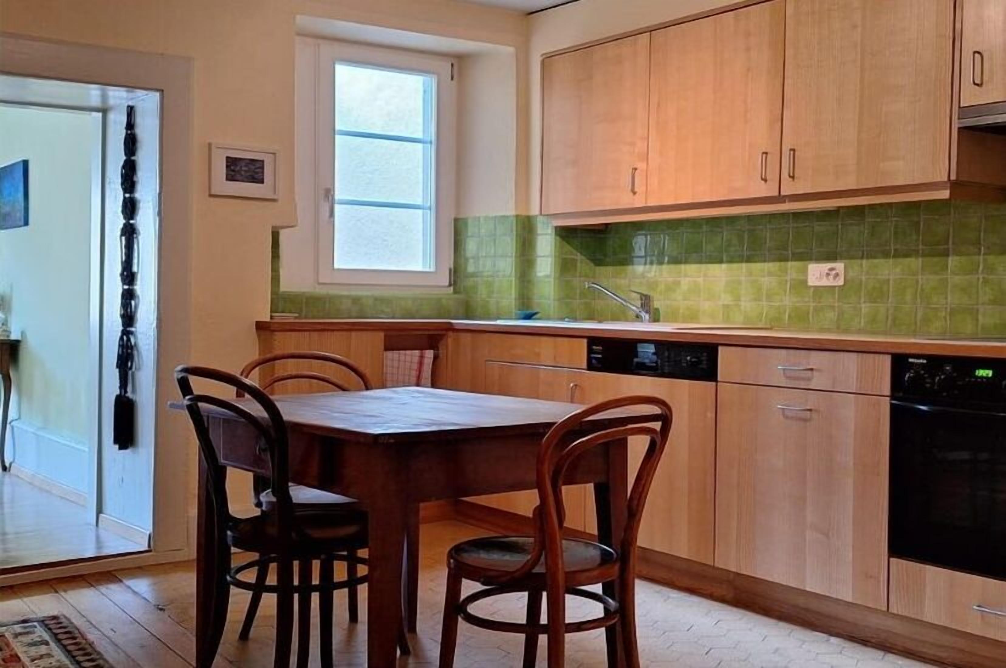 Een keuken met houten kastjes, een eettafel met stoelen, een raam en een vaatwasser.