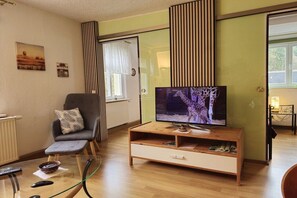 A living room with a television, a sofa, a glass coffee table, and a wooden entertainment unit. - Holiday apartment with 2 bedrooms (Bad Schandau)