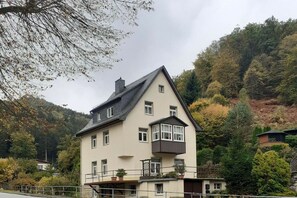 A two-story building with a balcony, surrounded by trees and hills. - Holiday apartment with 2 bedrooms (Bad Schandau)
