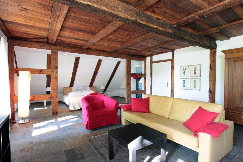 A room with a wooden ceiling, a sofa, a chair, a table, and a bed.
