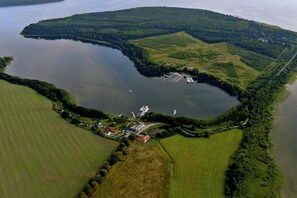 An aerial view of a lake surrounded by green fields and a small settlement with buildings and boats. - Holiday apartment with 1 bedroom (Alt-Schwerin)