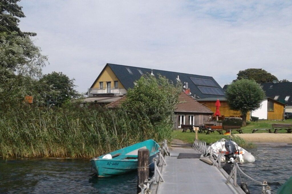 Ein Flusskai mit einem Boot, einer Holzsteganlage und einem Gebäude mit Solaranlage.
