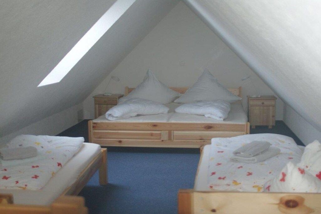 Quarto sótão pequeno e triangular, com uma cama de solteiro e duas mesas de cabeceira, cada uma com uma luminária.