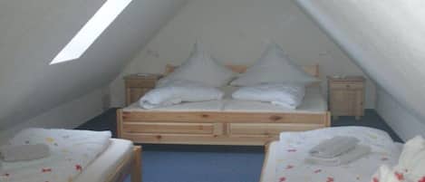 Quarto sótão pequeno e triangular, com uma cama de solteiro e duas mesas de cabeceira, cada uma com uma luminária.