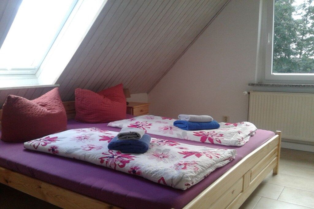 Een slaapkamer met een schuine kap, twee bedden met bloemenbeddengoed en een raam met uitzicht op bomen.