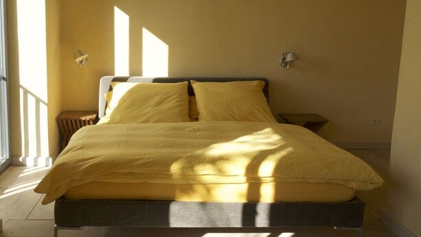 A bed with a yellow bedspread in a room with a window and two wall-mounted lamps. - Holiday apartment with 1 bedroom (Potsdam)