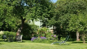 A grassy outdoor area with a tree, a bench, and a lounge chair. - Holiday apartment with 1 bedroom (Potsdam)