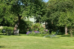 Et grønt udendørsområde med et træ, en bænk og en liggestol.