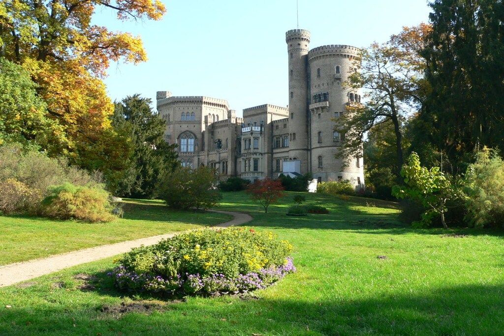 A castle with a central tower, surrounded by a well-maintained garden and a clear sky.