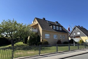 Una casa residencial con techo inclinado, un balcón y un asta de bandera.