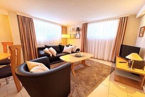 A modern living room with a sofa, a coffee table, a TV stand, and a dining area. - Holiday apartment with 2 bedrooms (Lübeck)