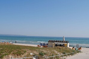 Een strandlocatie met een klein gebouw, mogelijk een café of restaurant, en een omheind gebied met strandstoelen.