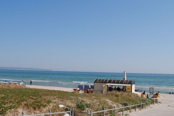 Un endroit situé en bord de mer, avec un petit bâtiment, peut-être un café ou un restaurant, et un espace clôturé avec des chaises de plage.