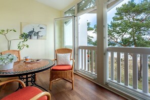 A balcony with wicker furniture, a table with a vase of flowers, and a painting on the wall. - Holiday apartment with 1 bedroom (Ostseebad Binz)