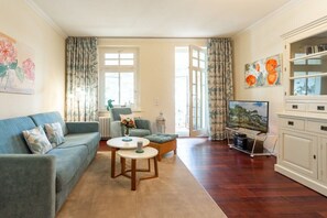 A living room with a sofa, a coffee table, a TV, and a bookshelf. - Holiday apartment with 1 bedroom (Ostseebad Binz)