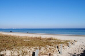 A beach with a clear sky, sandy shore, and a few people walking. - 1.5 in Residence Margarete (Ostseebad Binz)