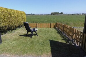 Eine Terrasse mit einem Stuhl, einem Holzzaun und einer Hecke.