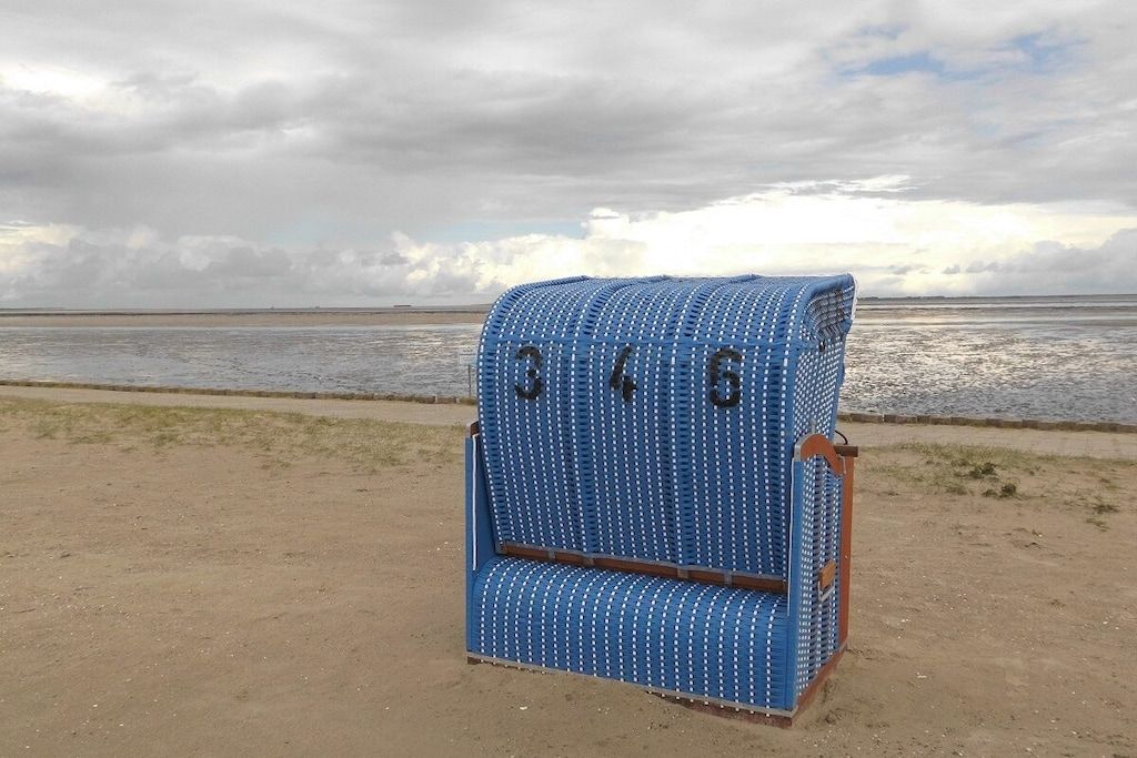 A blue, cylindrical, numbered object with the numbers 346 on it, placed on a sandy surface near a body of water.