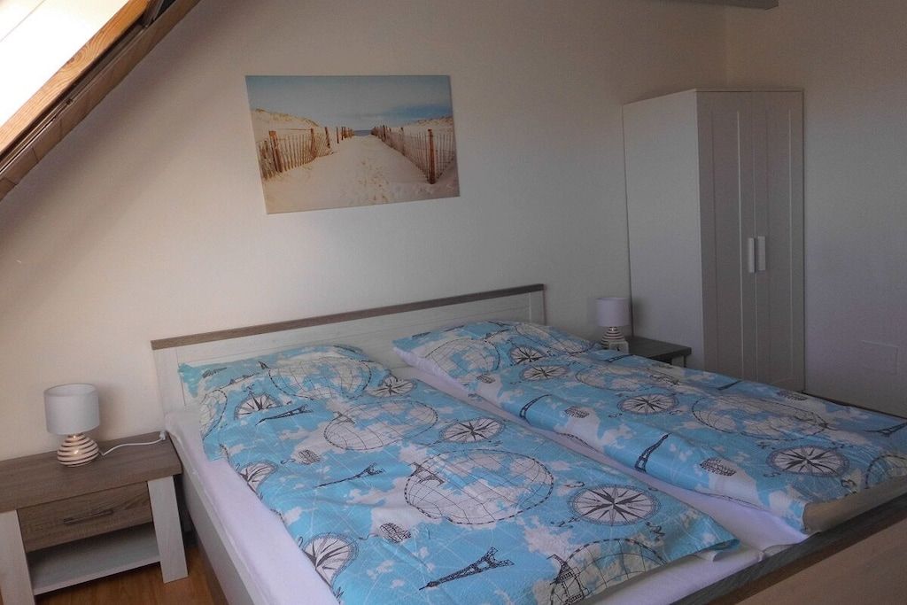 Quarto com cama, mesa de cabeceira, luminária, guarda-roupa e um quadro na parede.