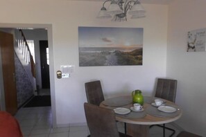 A dining area with a round table, chairs, a painting, and a door with a lock. - Holiday home with 2 bedrooms (Dornumersiel)