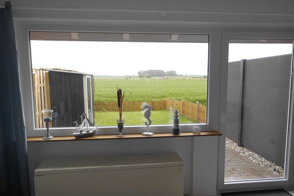 Een kamer met een groot raam dat uitkijkt op een gazon, een radiator eronder en een plank met decoratieve spullen.