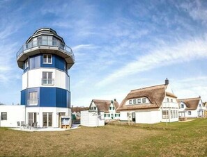 A lighthouse with a cylindrical tower, adjacent to a row of traditional houses with thatched roofs. - Holiday home in Breege with swimming pool (Breege)
