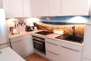 A modern kitchen with white cabinets, a black countertop, a stove, a sink, and a coffee maker. - Holiday home in Breege with swimming pool (Breege)