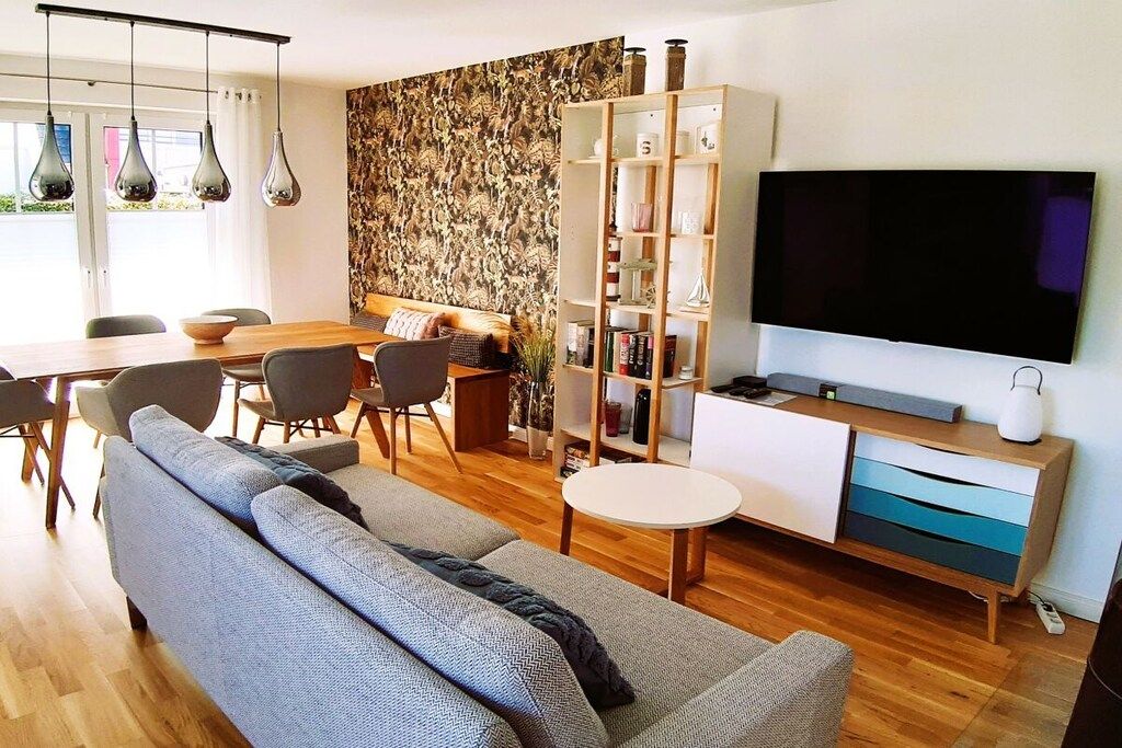 A modern living room with a sofa, dining table, chairs, a bookshelf, and a TV.