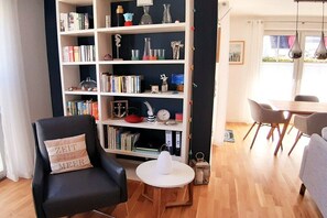 A modern living room with a bookshelf, a black armchair with a cushion, a round coffee table, and a dining area with a table and chairs. - Holiday home in Breege with swimming pool (Breege)